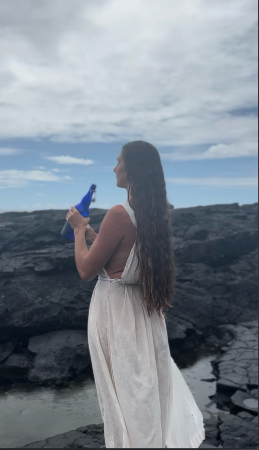 Woman holding a blue glass bottle on volcanic rock cliff